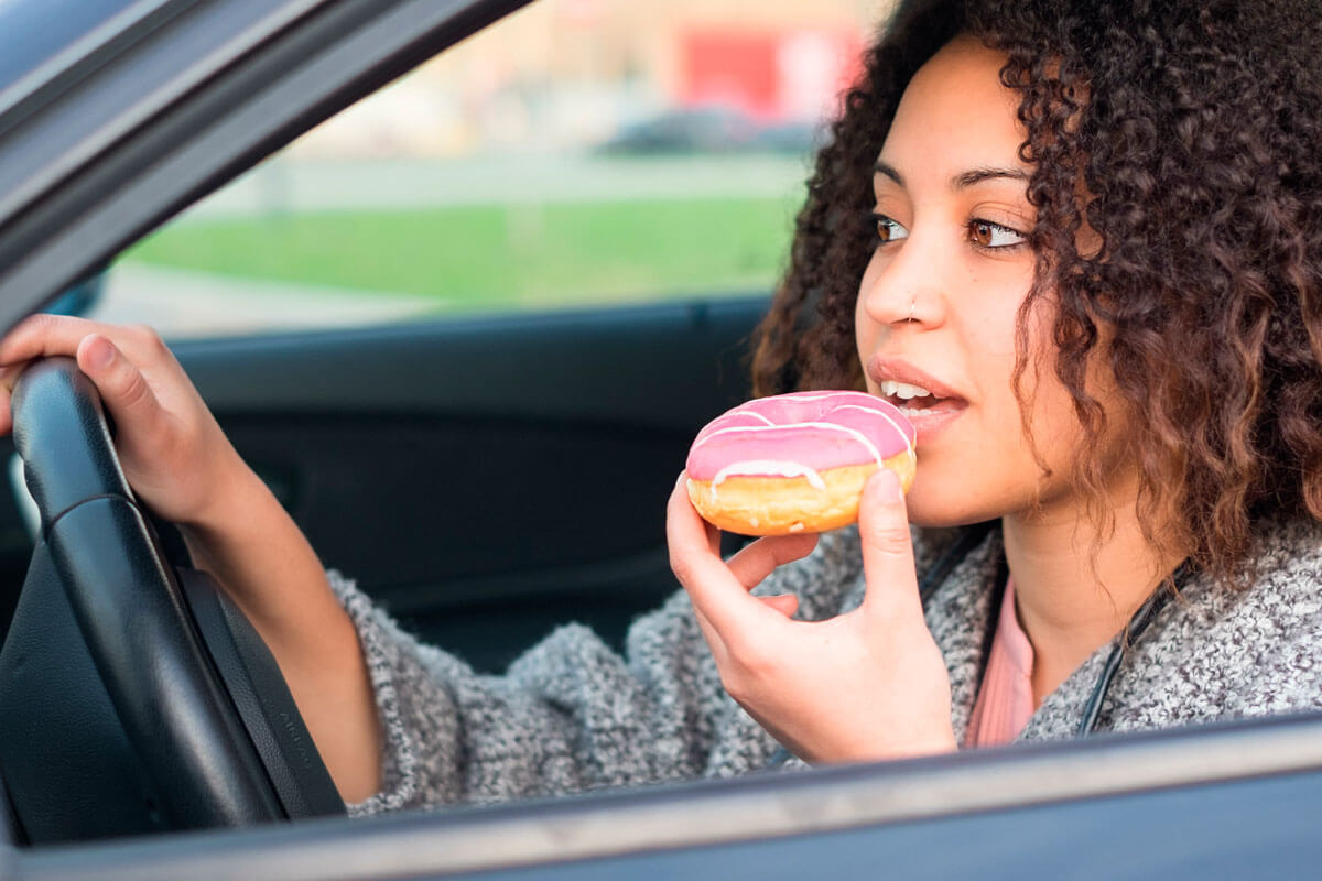 Frau isst am Steuer einen süßen Donut. Besonders Frauen neigen zu Stressessen.